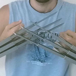 Peut inclure: Une personne portant un débardeur bleu tient une paire de griffes en métal argenté. Les griffes sont composées de plusieurs pièces de métal qui sont reliées entre elles.