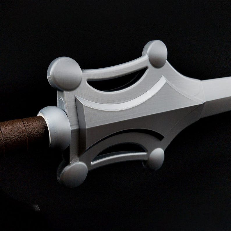 May include: A sword with a silver-colored crossguard featuring four rounded circular accents at the corners and a brown textured handle. The blade extends from the center of the guard, which has a smooth, metallic finish and visible layered lines.