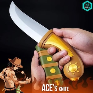 Op de afbeelding: Een rekwisietmes met een gebogen zilveren lemmet en een bruin en gouden handvat. Het handvat wordt door een hand vastgehouden. Het mes heeft een groene schede met gouden accenten. De tekst "ACE'S KNIFE" is zichtbaar.