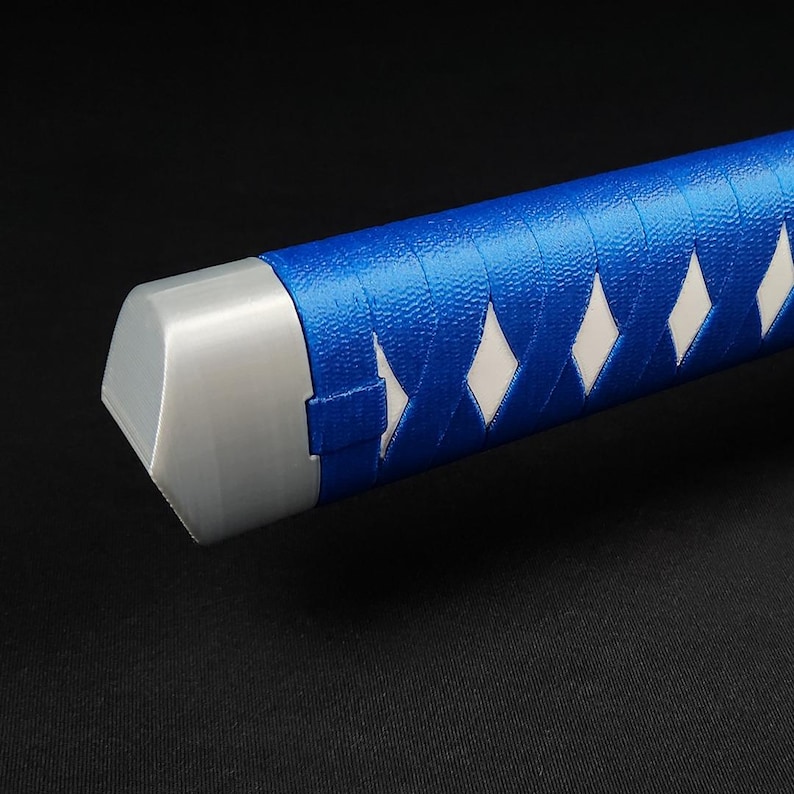 May include: Close-up of a katana handle. The handle is wrapped in textured blue material with white diamond-shaped accents. The end cap is silver and angular, contrasting with the blue. The background is black.