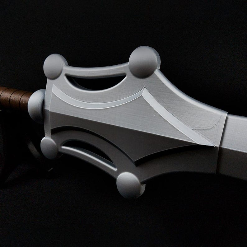 May include: A silver-colored sword with a wide, angular crossguard featuring four prominent circular accents. The blade extends from the center of the guard, and the handle is wrapped in brown material, showing a distinct metallic finish throughout.