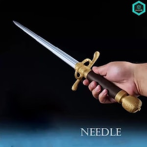 Op de afbeelding: Een zilverkleurig metalen zwaard met een puntig lemmet, een donkerbruin cilindrisch handvat en een sierlijke goudkleurige metalen stootplaat en pommel met ingewikkelde reliëfpatronen. Het woord NEEDLE staat onderaan in het wit gedrukt.