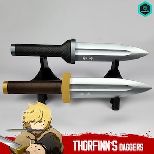 Op de afbeelding: Twee rekwisietendolken met zilveren bladen en zwarte en bruine handvatten worden tentoongesteld op zwarte standaards. De dolken hebben een punt en een bescherming. De tekst "THORFINN'S DAGGERS" staat onderaan de afbeelding.