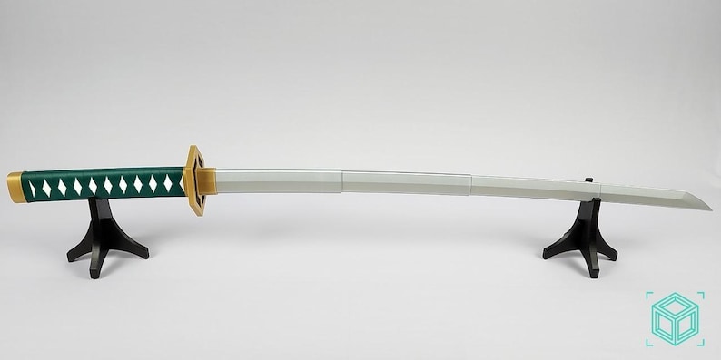 May include: A katana sword with a green handle featuring white diamond-shaped cutouts. The sword has a gold-colored handguard and a silver blade. It is displayed on two black stands against a white background.