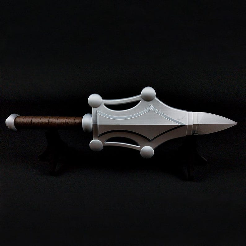 May include: A silver-colored prop weapon featuring a pointed blade with a wide, decorative guard adorned with four spherical accents. The handle is wrapped in a brown textured material, and the pommel is a smooth, rounded silver-colored cap.