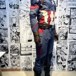 May include: A blue and red superhero costume with a star on the chest. The costume includes a jacket, pants, and boots. The boots are black with a brown leather strap.