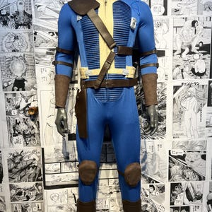 May include: A blue and brown jumpsuit with a leather belt and straps. The jumpsuit has a zipper in the front and a collar. The jumpsuit is worn by a mannequin.