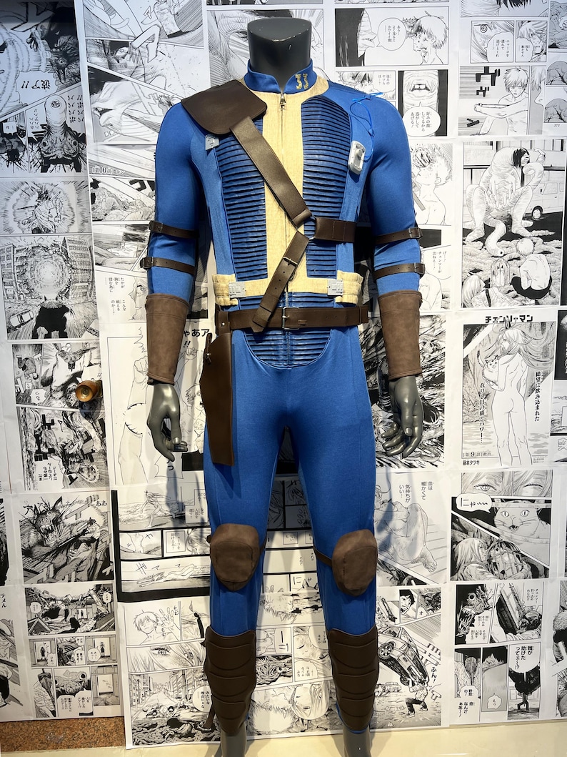 May include: A blue and brown jumpsuit with a leather belt and straps. The jumpsuit has a zipper in the front and a collar. The jumpsuit is worn by a mannequin.