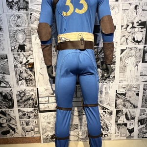 May include: A blue jumpsuit with brown leather accents and a gold number 33 on the back. The jumpsuit has a brown belt with a pouch on the front. The jumpsuit is on a mannequin.