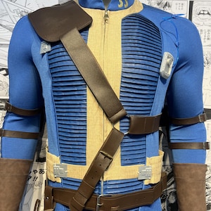 May include: A blue and tan jumpsuit with brown leather straps and a belt. The jumpsuit has a zipper in the front and a patch on the left shoulder. The jumpsuit is worn by a mannequin.