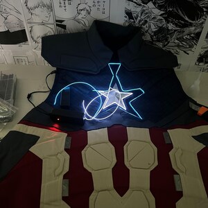 May include: A blue and red costume with a white star on the chest. The star is lit up with blue light. The costume is made of fabric and has a padded chest piece.
