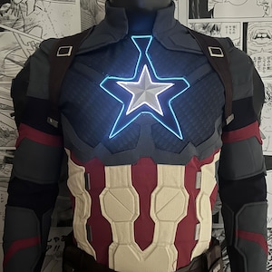 May include: A blue and red superhero costume with a white star on the chest. The star is illuminated with a blue light. The costume has a brown belt and a black and gray design on the arms.