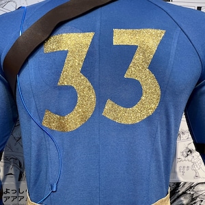 May include: A blue long-sleeved shirt with a brown strap and a gold glitter number 33 on the back.