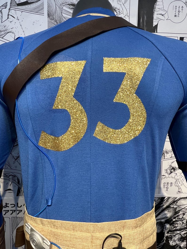 May include: A blue long-sleeved shirt with a brown strap and a gold glitter number 33 on the back.