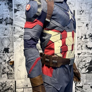 May include: A blue and red superhero costume with a brown leather belt and gloves. The costume has a star on the chest and a red, white, and blue shield on the arm.