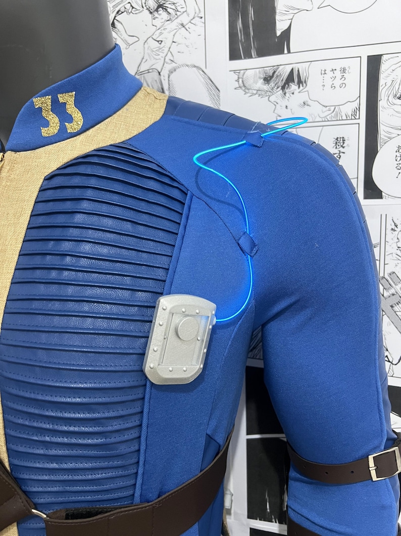 May include: A blue jumpsuit with a tan collar and a silver badge on the chest. The jumpsuit has a brown belt and a blue light cord running from the shoulder to the badge. The number "33" is embroidered on the collar in gold thread.