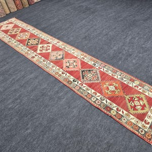 May include: A long, rectangular red runner rug with a repeating geometric pattern in cream, black, and orange. The rug has a detailed border with floral and geometric motifs, and is suitable for hallways or entryways.