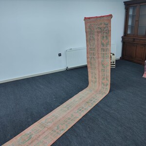Peut inclure: Un tapis long et étroit, de couleur rose et verte, avec un motif géométrique. Le tapis est posé sur un tapis gris foncé.
