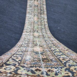 May include: A vintage runner rug with a floral pattern in shades of beige, brown, green, and blue. The rug has a distressed look and is made of a woven material.