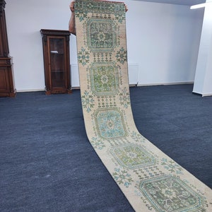 May include: A long, cream-colored rug with a geometric pattern in shades of green and blue. The rug has a traditional design with repeating squares and floral motifs.