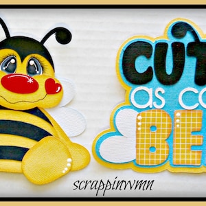 May include: A whimsical, cartoon-style bee and a sign that reads "Cute as can BEE." The bee is yellow and black with large eyes and red heart-shaped cheeks. The sign has blue and yellow accents.