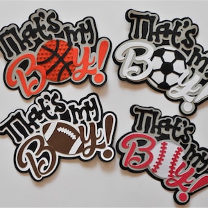 May include: Four paper cutouts with the text "That's my Boy!" in black and white with a red accent. Each cutout features a different sports ball: basketball, soccer ball, football, and baseball.