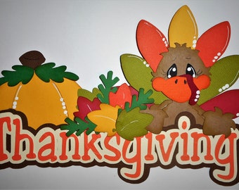 May include: A Thanksgiving themed paper craft with a brown turkey with a red beak and orange and yellow feathers, a pumpkin, and green leaves. The word "Thanksgiving" is written in orange and red letters.