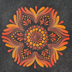 May include: A detailed mandala design in orange, brown, and yellow hues. The artwork features a central circle surrounded by layered petal-like shapes, set against a dark grey background. The design is created with small dots, creating a textured effect.