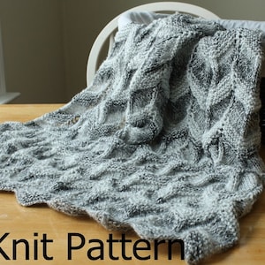 May include: A gray and white knitted blanket with a textured pattern. The blanket is draped over a chair and a wicker basket.