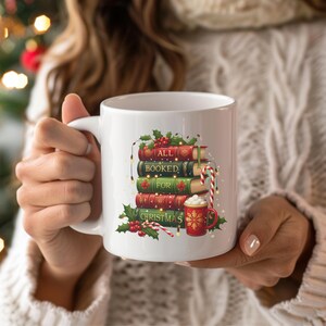 May include: White ceramic mug featuring a stack of books with the words "ALL BOOKED FOR CHRISTMAS." The books are red and green, decorated with holly and berries. A red mug with a gold design and a candy cane complete the festive design.