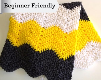 May include: A crocheted blanket featuring a chevron pattern in horizontal stripes of dark grey, bright yellow, and white yarn. A banner overlay in the upper left corner contains the black text "Beginner Friendly" in a serif font.