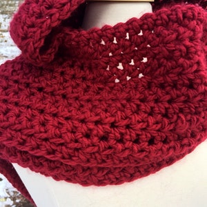May include: A red crocheted cowl with a hood. The cowl is made with a simple stitch pattern and has a soft, cozy feel.