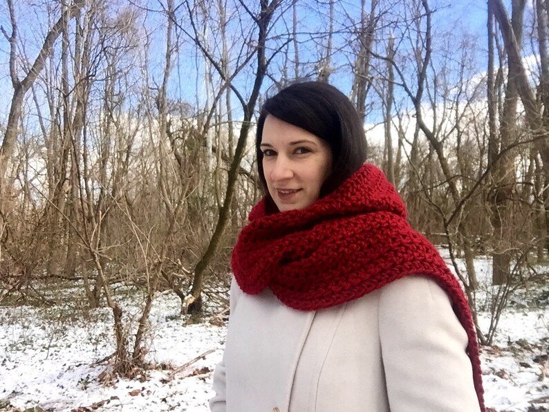 May include: A woman wearing a white coat and a long, red crocheted scarf in a snowy forest setting.