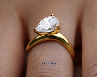 Könnte beinhalten: Ein goldener Ring mit einem birnenförmigen Diamanten. Der Ring befindet sich an einem Finger.