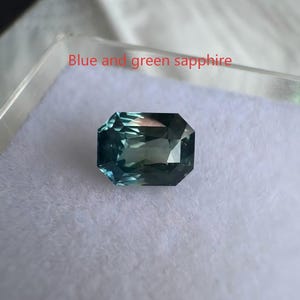 May include: A rectangular, faceted blue and green sapphire gemstone. The gem is set against a white background and is labeled "Blue and green sapphire". The sapphire has a deep, rich color and is cut to maximize light reflection.