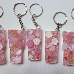 May include: Five pink resin keychain charms with silver key rings. Each charm features a different floral design with pink, white, and clear embellishments.