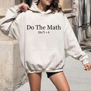 A person wearing a white hoodie with the text "Do The Math [9x7+4]" printed on it.