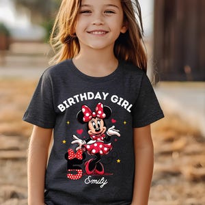 A young girl wearing a black t-shirt with a Minnie Mouse design and the text "Birthday Girl Emily" printed on it.