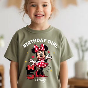 A young girl wearing a green t-shirt with a Minnie Mouse graphic and the text "Birthday Girl Emily" printed on it.