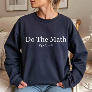 A person wearing a navy blue sweatshirt with the text "Do The Math [9x7+4]" printed on it.