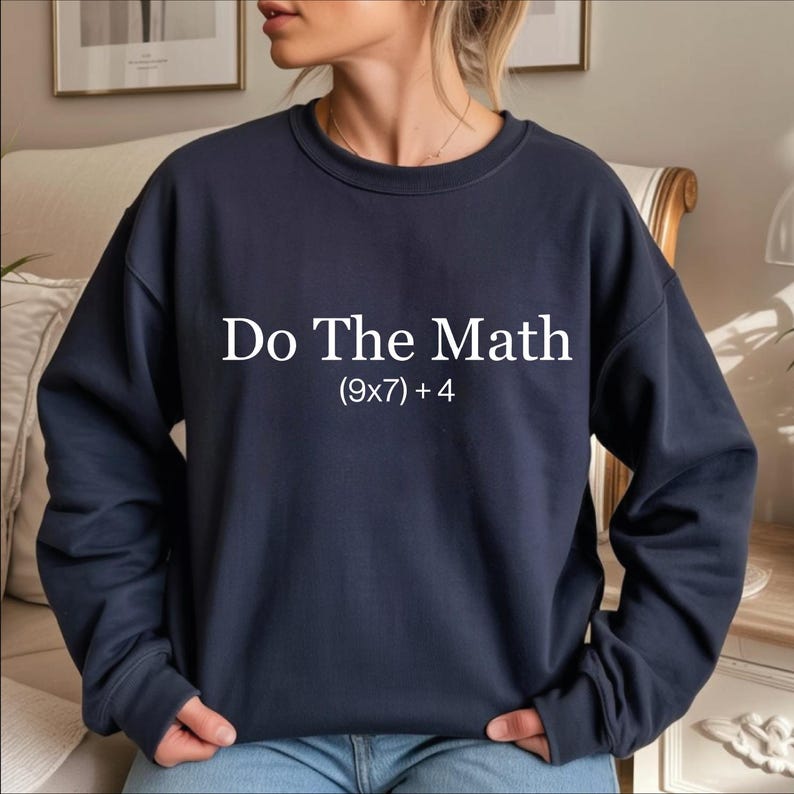 A person wearing a navy blue sweatshirt with the text "Do The Math [9x7+4]" printed on it.