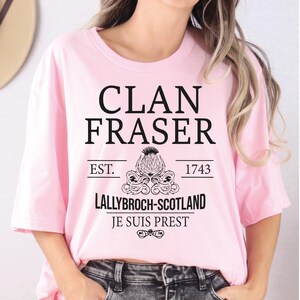 A woman wearing a pink t-shirt with text and graphics printed on it.