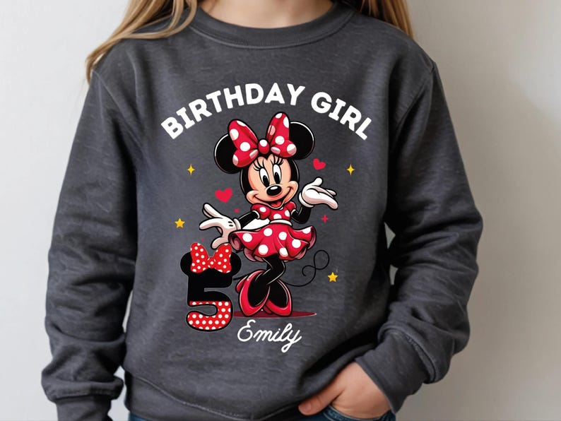 A young girl wearing a gray sweatshirt with a Minnie Mouse design and the text "Birthday Girl Emily" printed on it.