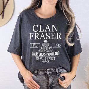 A woman wearing a grey t-shirt with white text and graphics printed on it.
