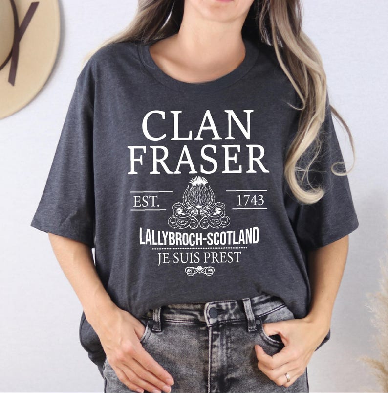 A woman wearing a grey t-shirt with white text and graphics printed on it.