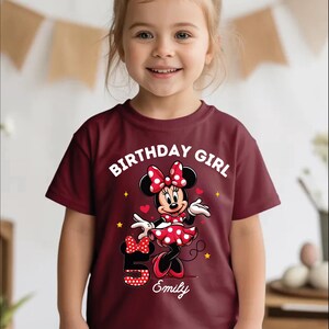 A young girl wearing a red t-shirt with a Minnie Mouse design and the text "Birthday Girl Emily" printed on it.