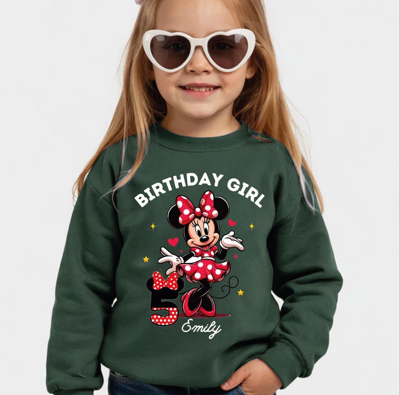 A young girl wearing a green sweatshirt with a Minnie Mouse design and the text "Birthday Girl" printed on it.