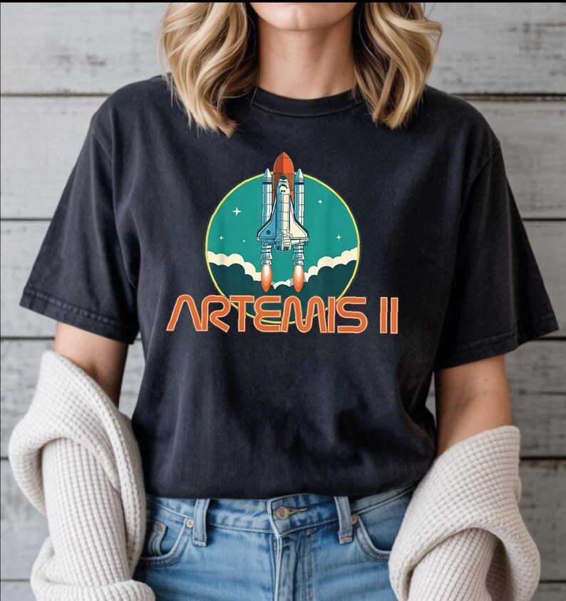 A woman wearing a black t-shirt with a graphic design of a space shuttle and the text "ARTEMIS II" printed on it.