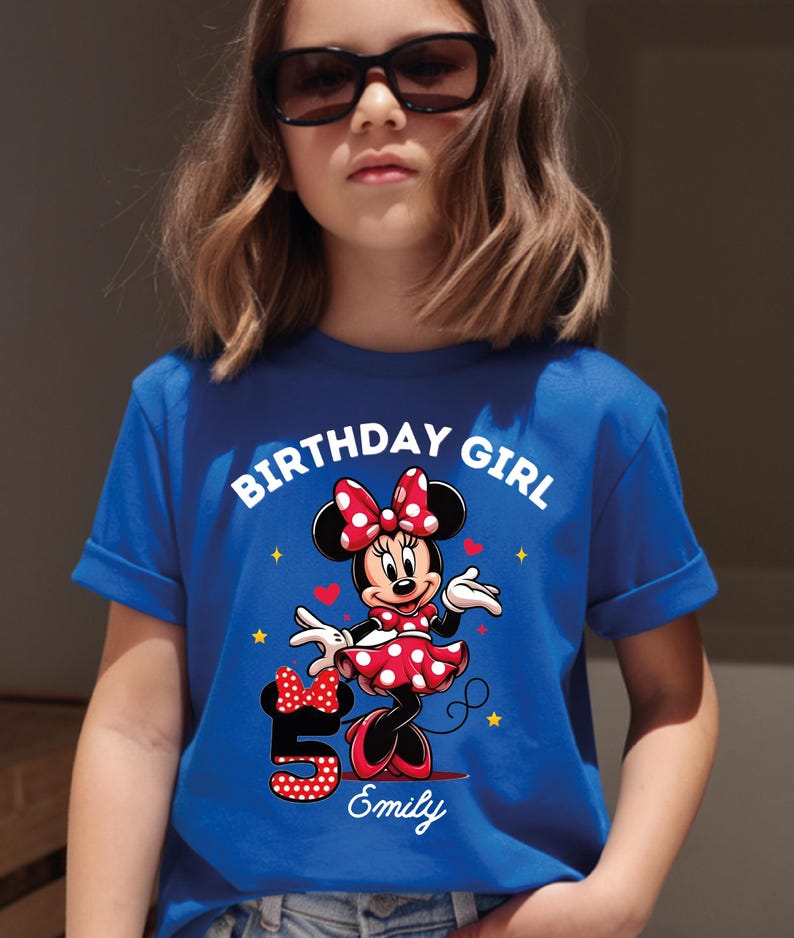 A young girl wearing a blue t-shirt with a Minnie Mouse design and the text "Birthday Girl Emily" printed on it.
