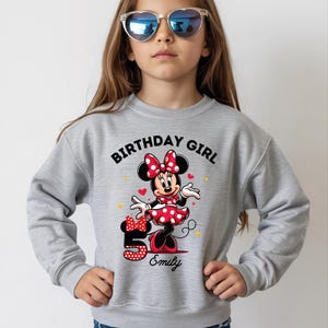 A young girl wearing a gray sweatshirt with a Minnie Mouse design and sunglasses, celebrating her 5th birthday.